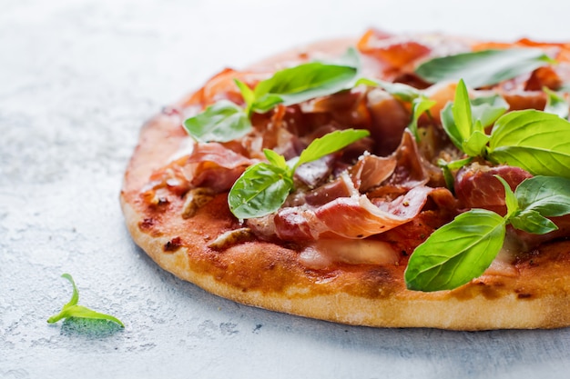 Homemade pizza with jamon, mozzarella and basil leaves on concrete old background. Selective focus