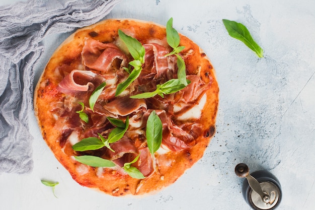 Homemade pizza with jamon, mozzarella and basil leaves on concrete old background. Top view.