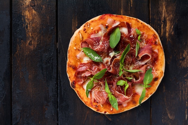 Homemade pizza with jamon, mozzarella and fresh basil leaves  