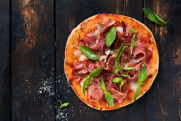 Homemade pizza with jamon, mozzarella and fresh basil leaves  