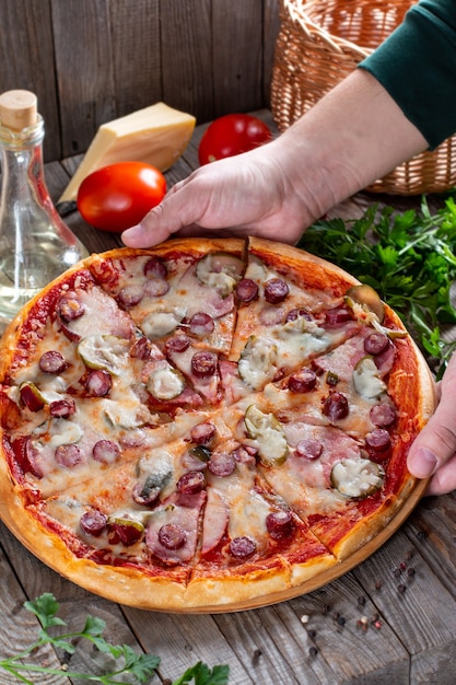 Homemade pizza with sausage, pickles, tomato and cheese on a table. Tasty food