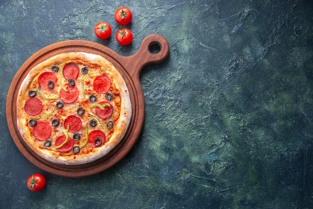 Homemade pizza on wooden cutting board and tomatoes on isolated dark surface