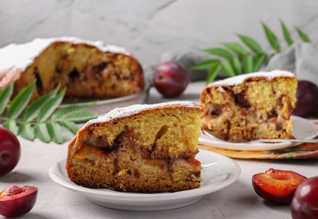 Homemade plum pie with a cut pieces on a plate on a light background closeup