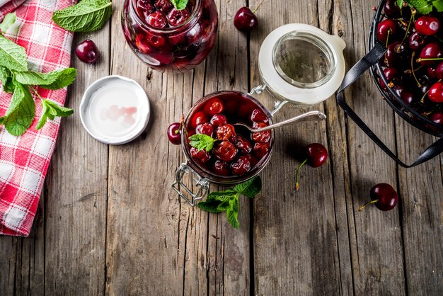 Homemade preserved cherry and mint jam, with fresh cherries on rustic old wooden background copy space above