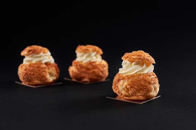 Homemade profiteroles with cream on black background.