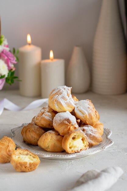 Homemade profiteroles with cream in a gray plate on a white table. Basket with fresh flowers