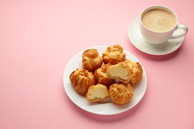 Homemade profiteroles with cream on plate with cup of coffee on pink background Fresh baked golden profiterole Top view