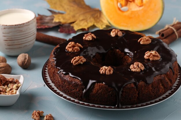 Homemade pumpkin muffin decorated with chocolate icing and walnuts on a light blue