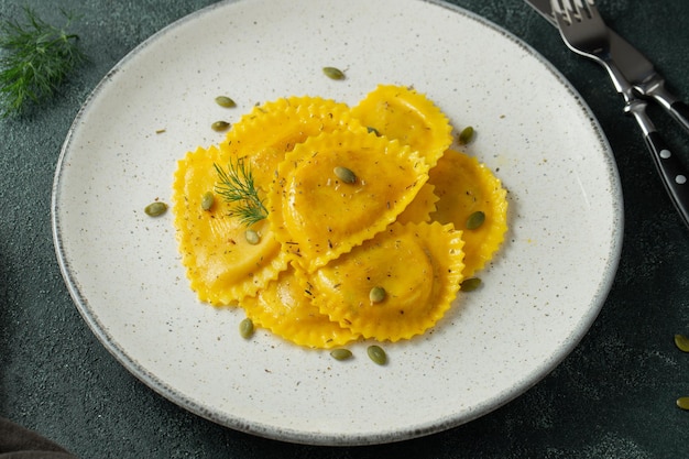 Homemade pumpkin ravioli with butter on a dark concrete background top view