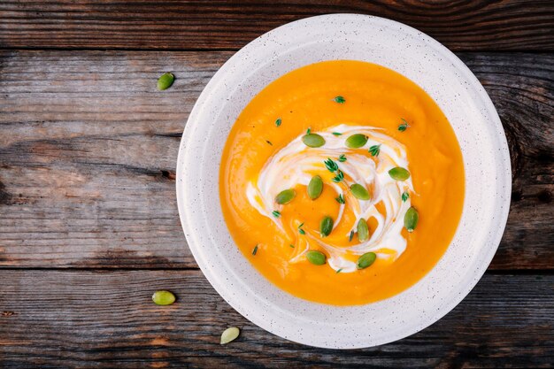 Homemade pumpkin soup with cream and seeds on wooden background