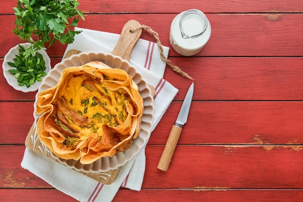 Homemade quiche or tart with slices of bacon and leeks with tortilla instead of dough on wooden cutting board on old red wooden background Quiche open tart traditional French cuisine Top view