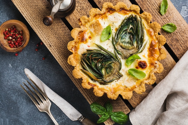 Homemade quiche tart with with artichoke on light wooden background.