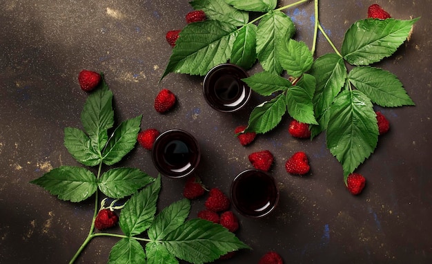 Homemade raspberry liqueur with fresh berries decorated green leaves brown table background top view