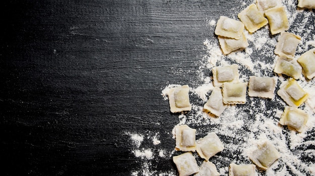 Homemade ravioli with flour. On the black table with flour. Free space for text . Top view