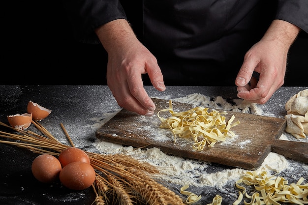 Homemade raw noodles made from flour, egg on wooden bowl on black