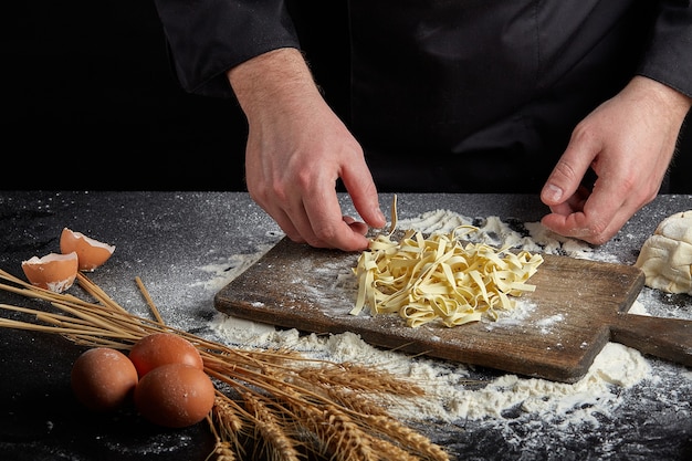 Homemade raw noodles made from flour, egg on wooden bowl on black