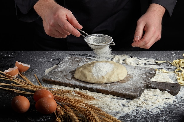 Homemade raw noodles made from flour, egg on wooden bowl on black