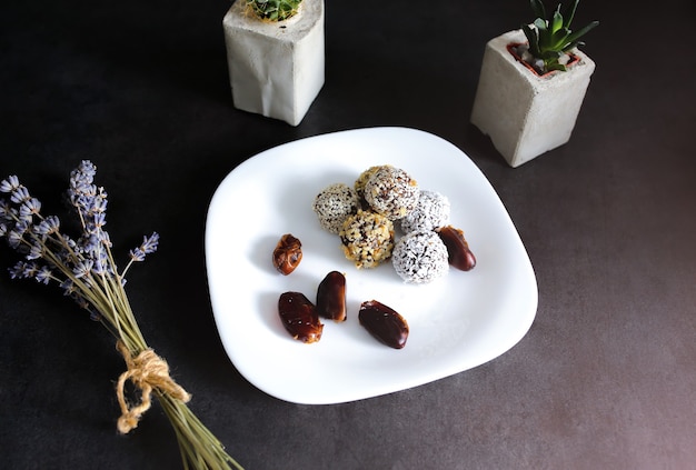 Homemade raw truffles with cocoa, nuts, coconut and dates on white plate and grey table. Lavender and succulents in concrete vases on background. Vegan, organic and healthy candy sweets.