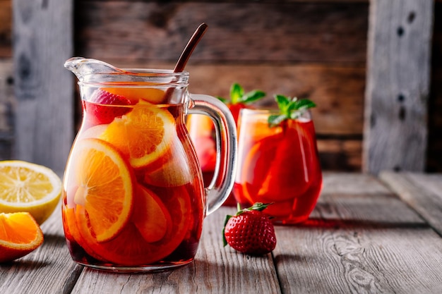 Homemade red wine sangria with orange apple strawberry and ice in pitcher and glass on rustic wooden background