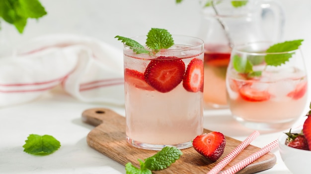 Homemade refreshing strawberry lemonade in pitcher and glass on wooden board