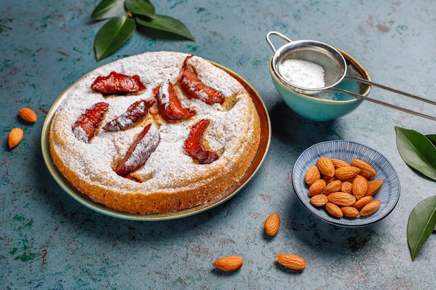 Homemade rustic plum cake with powdered sugar and almond, top view