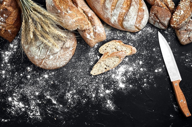 Homemade rye bread sprinkled with flour and various grains and seeds on a black background with spikelets of wheat or rye and oats