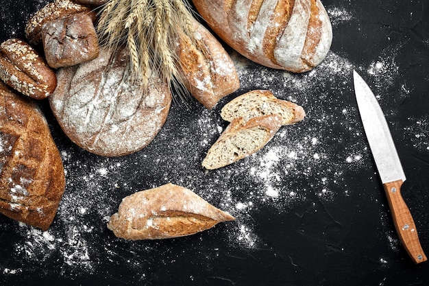 Homemade rye bread sprinkled with flour and various grains and seeds on a black background with spikelets of wheat or rye and oats