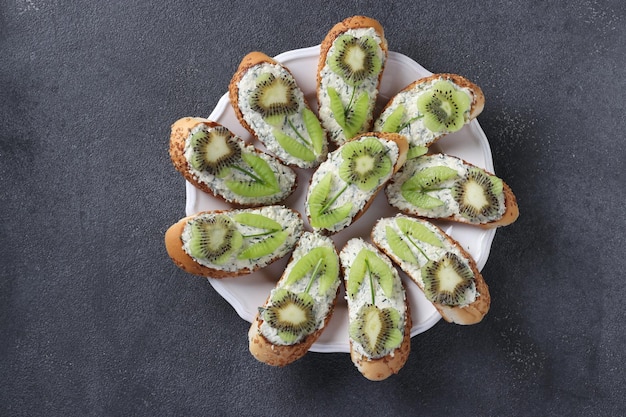 Homemade sandwiches with kiwi cream cheese and garlic on a round plate on a gray background Top view