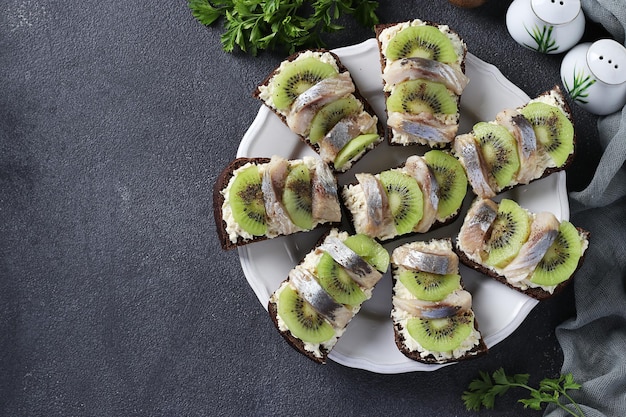 Homemade sandwiches with kiwi herring cream cheese and garlic on dark gray background Space for text