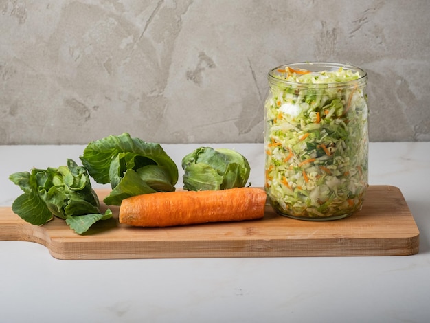 Homemade sauerkraut in a glass jar on a gray table.Cut green cabbage and carrots for cabbage soup.