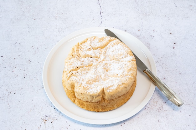 Homemade Savoie cake on a pretty white porcelain dish with jam in a jar