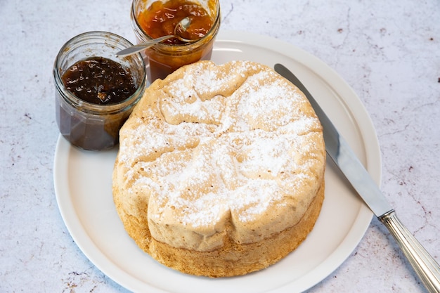 Homemade Savoie cake on a pretty white porcelain dish with jam in a jar