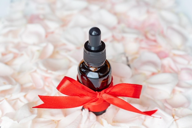 Homemade skincare natural rose essential oil product on Pink rose petals background in cosmetic dark glass bottle with dropper for moisturizing skin Unbranded package mockup