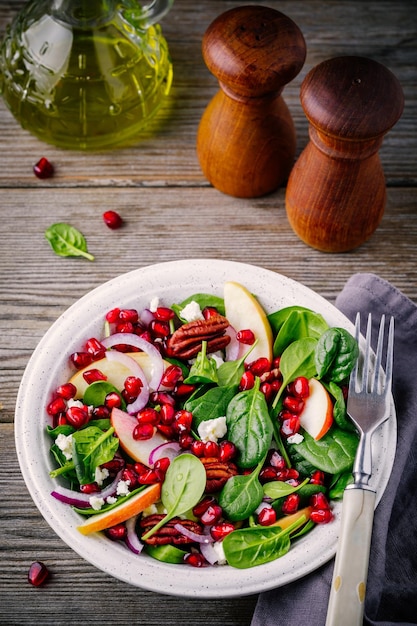 Homemade spinach apple pecan red onion salad with goat cheese and pomegranate on wooden background