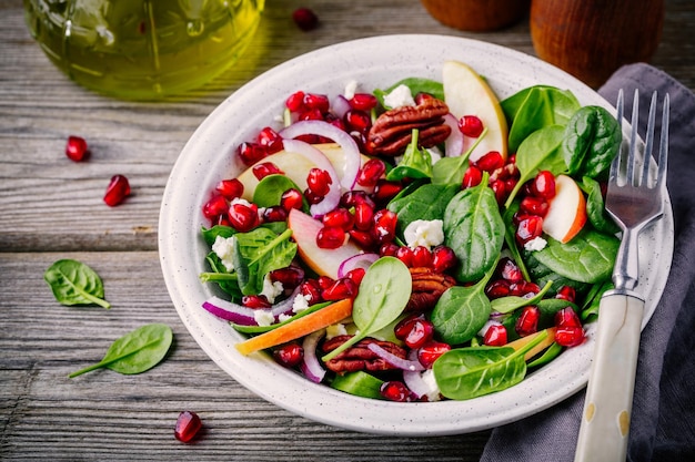 Homemade spinach apple pecan red onion salad with goat cheese and pomegranate on wooden background