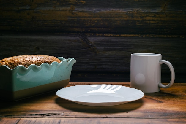 Homemade sponge cake in blue ceramic mold white cup and white plate on wooden table