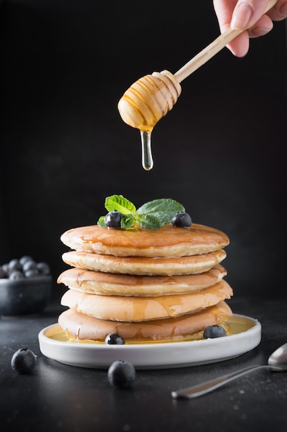 Homemade stack of pancakes with blueberry honey and mint in modern plate on black