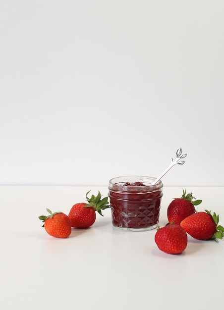 Homemade strawberry preserves or jam in a mason jar surrounded by fresh organic strawberries Selective focus with white background