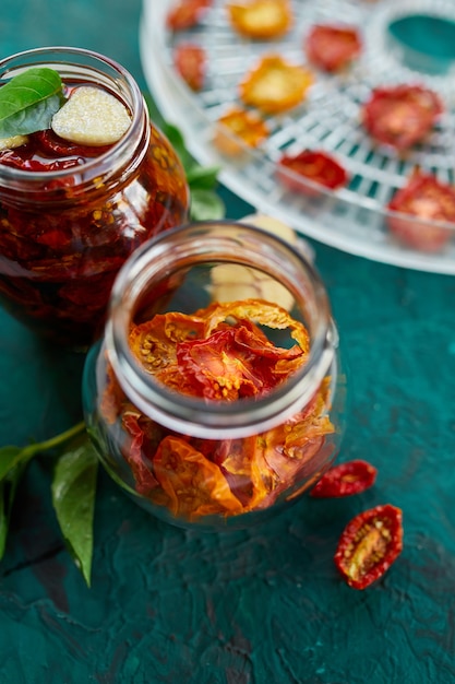 Homemade sun dried tomatoes with herbs, garlic in olive oil in a glass jar on dark green background. Top view. Print for kitchen