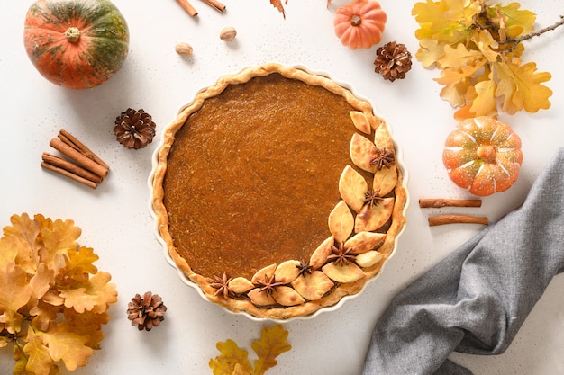 Homemade tasty pumpkin pie with autumn decorations and leaves for thanksgiving day on white