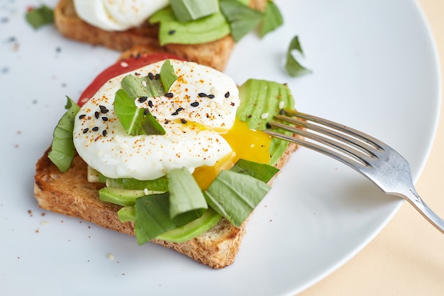 Homemade toast with avocado, poached eggs, tomato and seeds