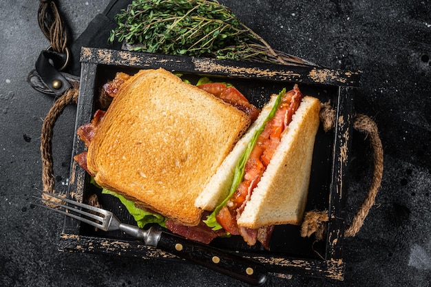 Homemade toasted BLT sandwich with bacon tomato and lettuce in wooden tray Black background Top view