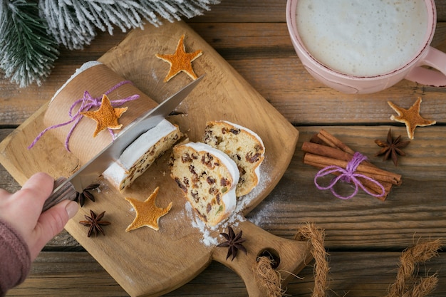 Homemade traditional Christmas dessert stollen with dried berries, nuts and powdered sugar on top stands on rustic wooden table