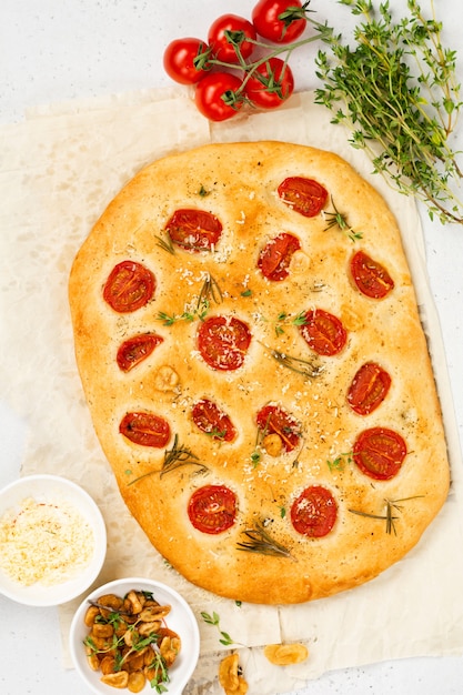 Homemade traditional Italian bread baking with cherry tomatoes, parmesan and rosemary on rustic light table wall. Top view.