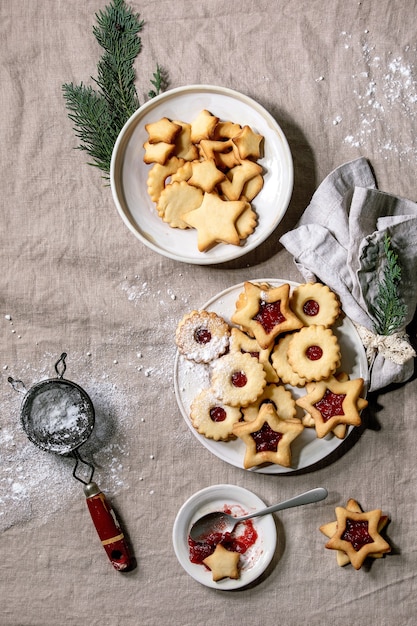 Homemade traditional Linz shortbread biscuits cookies with red jam and icing sugar on ceramic plate over linen tablecloth.