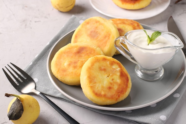 Homemade traditional Ukrainian dish syrniki with sour cream on grey plate on light background Cottage cheese pancakes