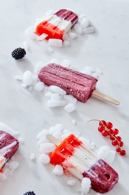 Homemade tricolor berry popsicles with ice and berries on marble background . Copy space for text.