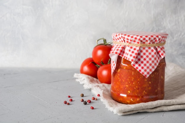 Homemade vegetable sauce adjika with tomatoes in jar on light background Closeup Space for text