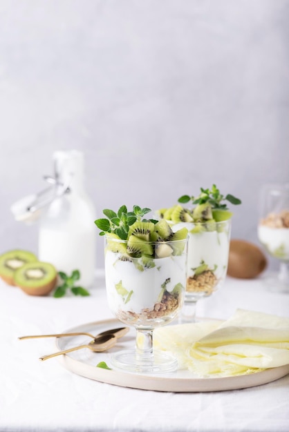 Homemade yogurt with fresh kiwi, muesli and mint on the white background, selective focus image