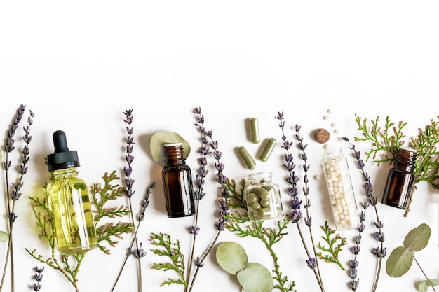 Homeopathy eco alternative medicine concept - classical homeopathy pills, thuja, eucalyptus, lavender essential and aroma oil and healing herbs and on white wall. Flatlay. Top view. Copyspace